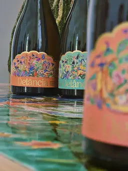 Bottles of the Delância botanical sparkling wine range arranged on a colourful reflective table setup