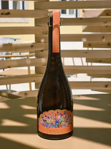 A bottle of Delância orange botanical sparkling wine on a sunlit outdoor terrace table