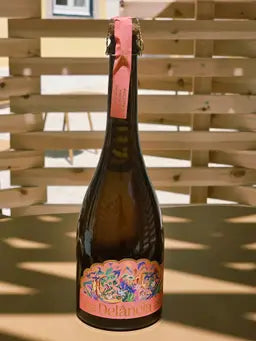 A bottle of Delância rosé botanical sparkling wine on a sunlit outdoor terrace table