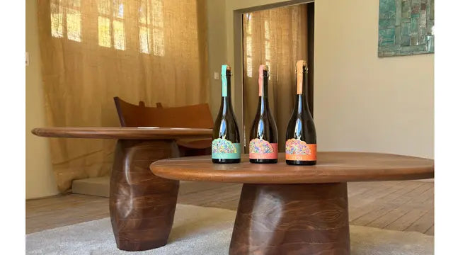 Three bottles of the Delância botanical sparkling wine range displayed on an indoor wooden table