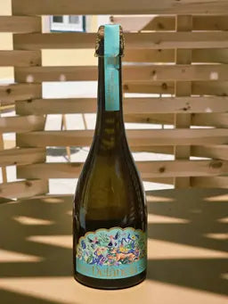 A bottle of Delância white botanical sparkling wine on a sunlit outdoor terrace table